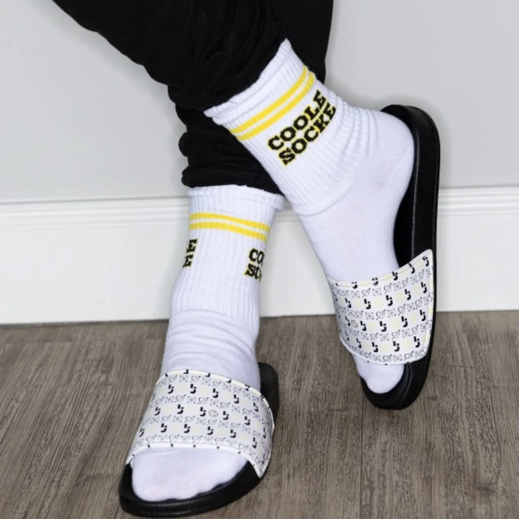 Feet in white “Coole Socke” socks and Logic Joe slides on the office’s wooden floor